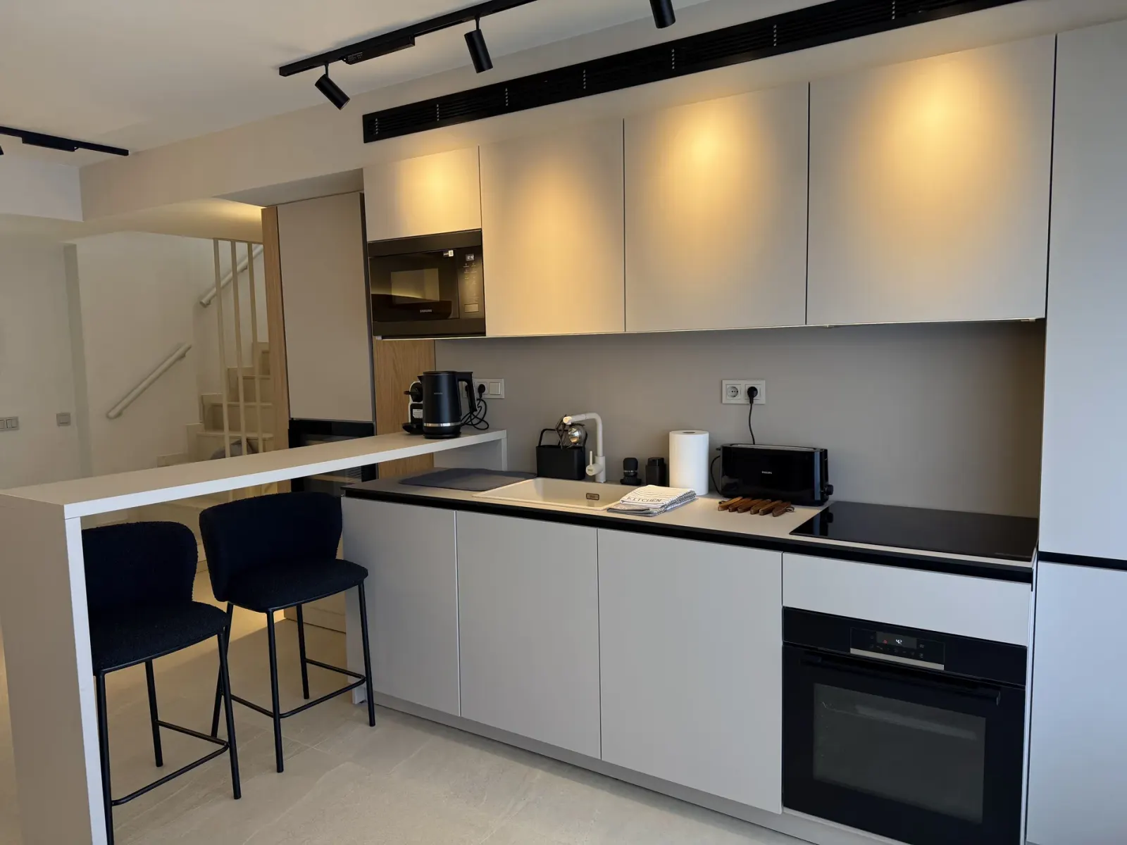 Cocina abierta con barra, muebles blancos y focos de carril